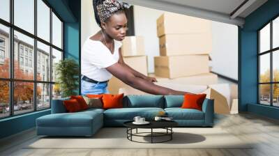 Afro american Woman packing and unpacking belongings in a carton box when moving home. Wall mural